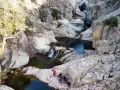 Un gruppo di escursionisti ammira un canyon con cascate e pozze d'acqua cristallina. Uno di loro, con un giubbotto rosa acceso, sembra dire "bau mela!" alla natura.
