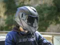 Casco da moto nero con visiera riflettente, che offre una sensazione di pressione sulla fronte. Indossato da una persona con giacca blu e nera.