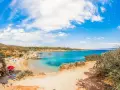 Spiaggia Lazzaretto ad Alghero: sabbia dorata, acque cristalline e macchia mediterranea sotto un cielo azzurro con nuvole bianche.