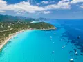 Spiaggia di Chia, Sardegna: acque cristalline che sembrano mari pintau, con barche a vela e un litorale affollato.