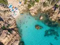 Vista aerea della spiaggia di Cala Coticcio, con bagnanti che si godono le acque cristalline e ombrelloni colorati sulla sabbia dorata.