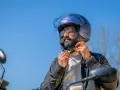 Uomo con barba e occhiali da sole che regola il cinturino di un casco da moto blu iridescente. La corretta misura casco moto è fondamentale per la sicurezza.