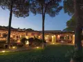 La sorgente Villasimius: un ristorante con tavoli all'aperto illuminati da luci soffuse, circondato da pini e un prato curato.