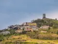 Il castello di Osilo domina un borgo colorato su una collina verdeggiante, sotto un cielo azzurro.