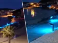 Passeggiata illuminata da luci blu sul lungomare di Golfo Aranci sera, con palme e case sullo sfondo.