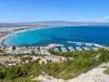 Vista panoramica della spiaggia del Poetto con mare turchese, porto turistico e saline rosa sullo sfondo.