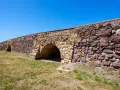 Antico ponte romano a Sant'Antioco, con archi in pietra e un muro imponente sotto un cielo azzurro.