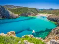 La splendida spiaggia di Buggerru, con acque cristalline e rocce imponenti, invita al relax. Una barca bianca solca il mare turchese.