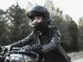 Woman in black leather jacket and helmet riding a motorcycle outdoors.
