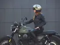 Donna in giacca di pelle e casco dorato, seduta su una moto verde. Non è chiaro dove si buttano i caschi da moto, ma questo è un ottimo esempio di come indossarli.