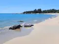 Spiaggia di Lido di Orrì con rocce scure bagnate dall'acqua cristallina e sabbia dorata.