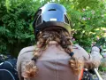 Donna con casco nero e capelli raccolti in due trecce, pronta per legare il casco alla moto.