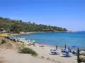Spiaggia di Porto Frailis con ombrelloni colorati, lettini blu e gente che si gode il mare cristallino sotto il sole.