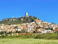 La **posada di sera** si staglia su una collina rocciosa, con case colorate e una torre medievale sotto un cielo azzurro.