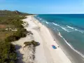 L'oasi di Bidderosa, una spiaggia sarda con sabbia chiara, vegetazione mediterranea e mare turchese, accoglie bagnanti sotto ombrelloni colorati.