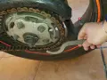 Mano con chiave inglese che lavora sulla catena di una moto, mostrando come tirare la catena della moto per la manutenzione.