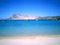Spiaggia di Cala Suaraccia, mare cristallino, montagne sullo sfondo e barche in lontananza. Come arrivare: goditi il panorama!