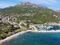 Vista aerea del centro storico di Santa Maria Navarrese, con case arroccate sulla collina, un porto turistico pieno di barche e il mare cristallino.