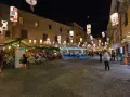 Serata ad Alghero: ristoranti all'aperto illuminati da lanterne, gente che passeggia e cena.