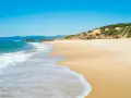 Onda bianca accarezza la sabbia dorata della spiaggia di Scivu, sotto un cielo azzurro intenso.