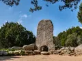 La tomba dei giganti in Sardegna, un imponente monolito di granito con un arco, circondato da pietre antiche e vegetazione rigogliosa sotto un cielo azzurro.