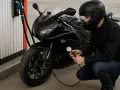 Motociclista controlla la pressione gomme moto 125 con un manometro. La moto è nera, parcheggiata vicino a una pompa di benzina.