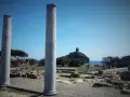 Colonne antiche nel **sito archeologico** di Nora, con una torre in lontananza su un'isola rocciosa.