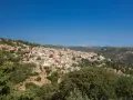 Panoramica di Seulo, Sardegna, con case colorate arroccate su una collina verdeggiante sotto un cielo azzurro.