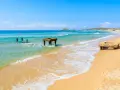 Spiaggia di Chia, Cagliari. Resti di antiche strutture in mare e sulla sabbia dorata, con acque turchesi e cielo azzurro.
