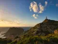 Faro solitario su una collina rocciosa, con il mare e le nuvole al tramonto. Un paesaggio mozzafiato di Nebida, Sardegna.