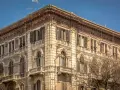 Angolo del **Palazzo Accardo a Cagliari**, con facciata in pietra chiara, balconi in ferro battuto e finestre con persiane.