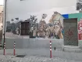 Un grande murale colorato decora un edificio in un paese, con volti, un cavallo e bandiere. Un'opera d'arte che racconta storie di un paese, murales in Sardegna.