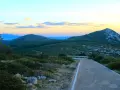 Strada panoramica verso il monte Doglia al tramonto, con colline verdi e cielo colorato.