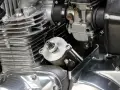 Dettaglio del motore di una moto: il test del motorino di avviamento è in primo piano, con il carburatore e le alette di raffreddamento visibili.