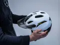 Mani che tengono la calotta esterna di un casco da bici bianco con visiera scura e logo Dainese.