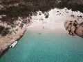 Una persona celebra la bellezza di Cala Soraya, con acque cristalline e rocce rosse. Una barca è ormeggiata.