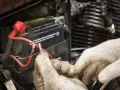 Mani guantate lavorano sulla batteria 12V della moto, forse per il tempo di ricarica.