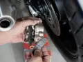Mani che sostituiscono pastiglie cristallizzate su una moto. Si vede la pinza del freno e il disco.