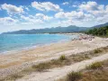 Spiaggia affollata con ombrelloni e gente che si gode il sole. Il nuoro mare azzurro lambisce la costa, con montagne verdi sullo sfondo.