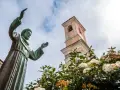 Statua di San Francesco con campanile e fiori. Il **Nuoro significato** di questo luogo è legato alla spiritualità e alla natura.
