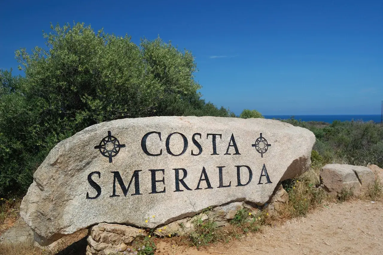 Masso con scritta "COSTA SMERALDA" in Sardegna, dove il mare azzurro incontra la macchia mediterranea.