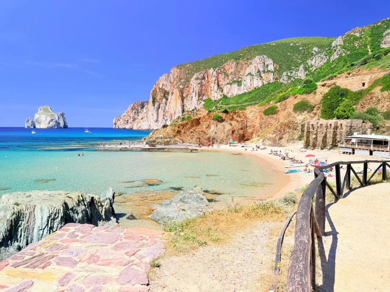 Spiaggia di Masua con acque cristalline, scogliere imponenti e il Pan di Zucchero all'orizzonte. Relax e natura incontaminata.