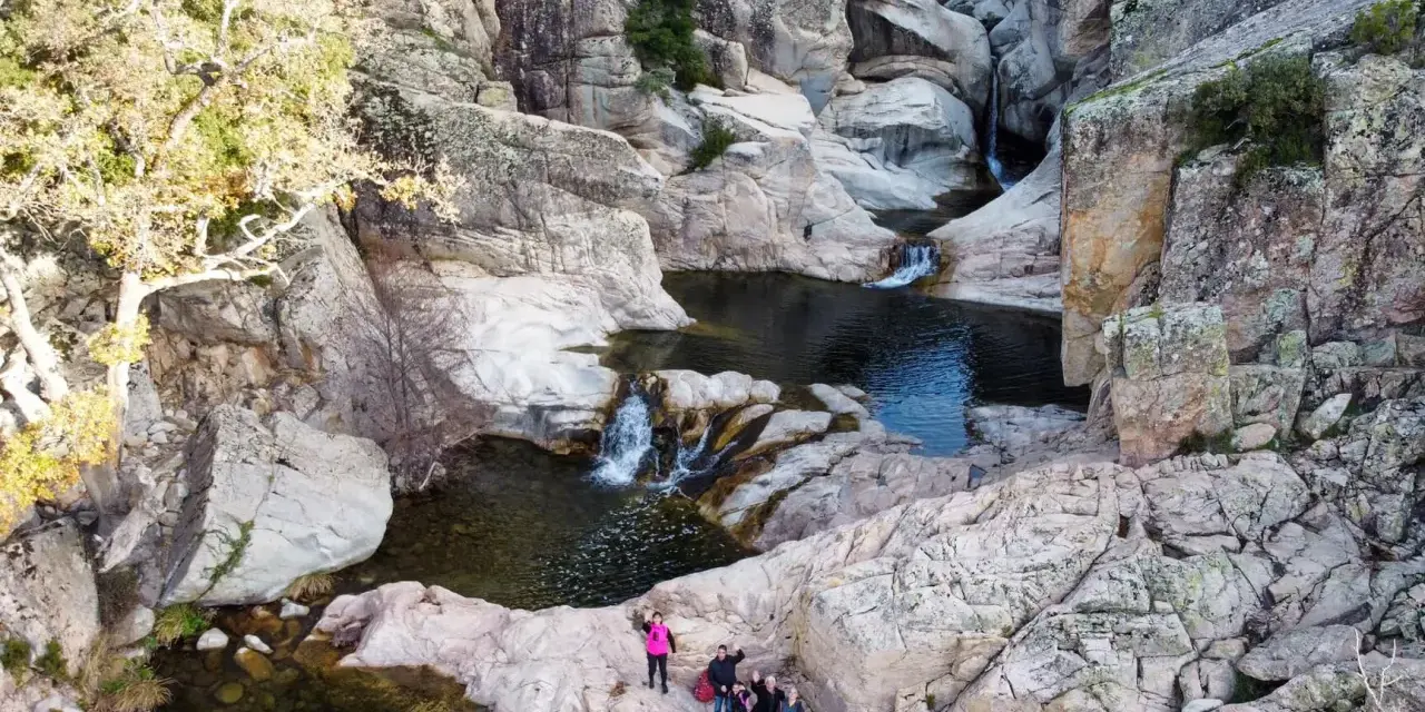 Un gruppo di escursionisti ammira un canyon con cascate e pozze d'acqua cristallina. Uno di loro, con un giubbotto rosa acceso, sembra dire "bau mela!" alla natura.
