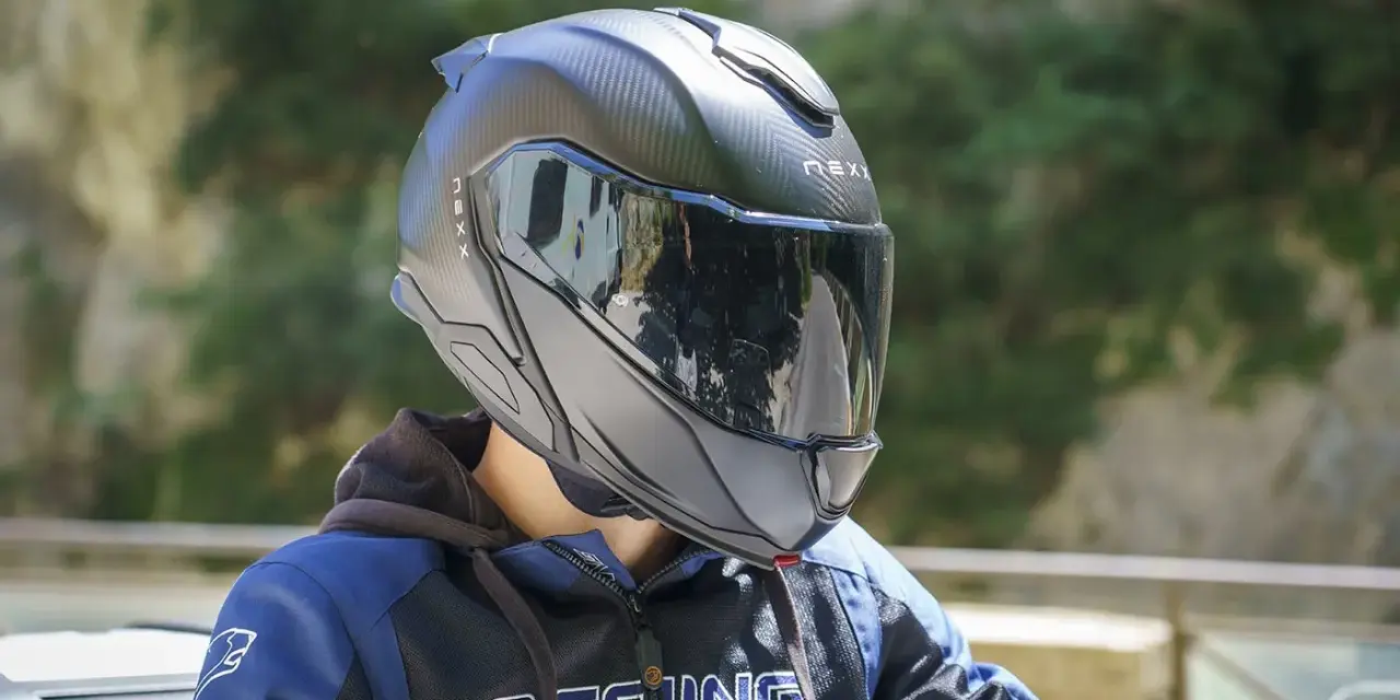 Casco da moto nero con visiera riflettente, che offre una sensazione di pressione sulla fronte. Indossato da una persona con giacca blu e nera.
