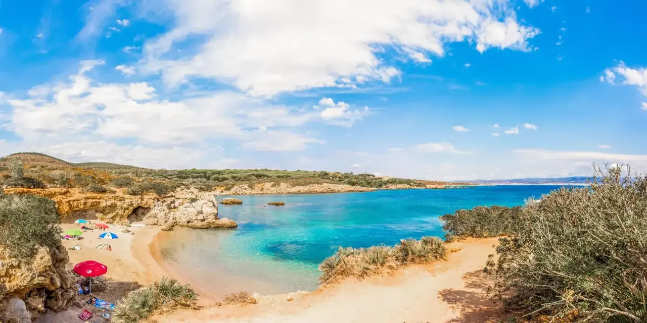 Spiaggia Lazzaretto ad Alghero: sabbia dorata, acque cristalline e macchia mediterranea sotto un cielo azzurro con nuvole bianche.