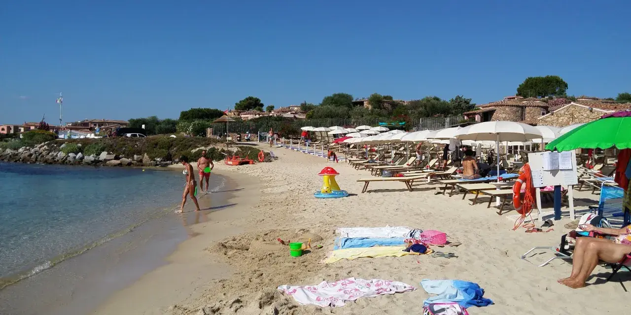 A sunny beach with people walking in the shallow water and lounging under umbrellas.