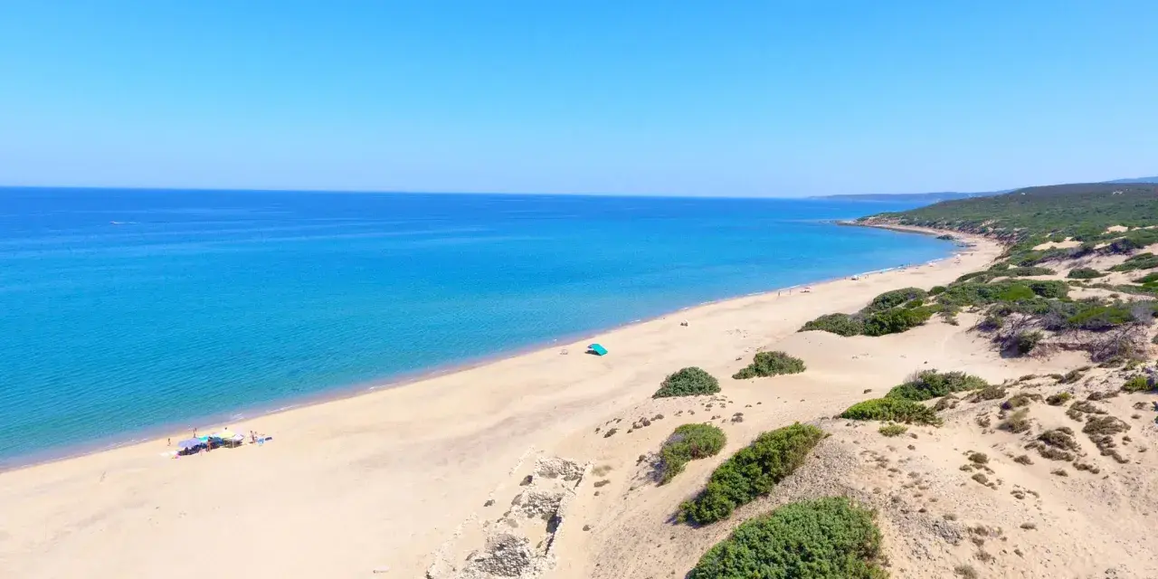 Vasta spiaggia di sabbia dorata, mare azzurro e vegetazione mediterranea sulla spiaggia di Piscinas. Rovine antiche emergono dalla sabbia.