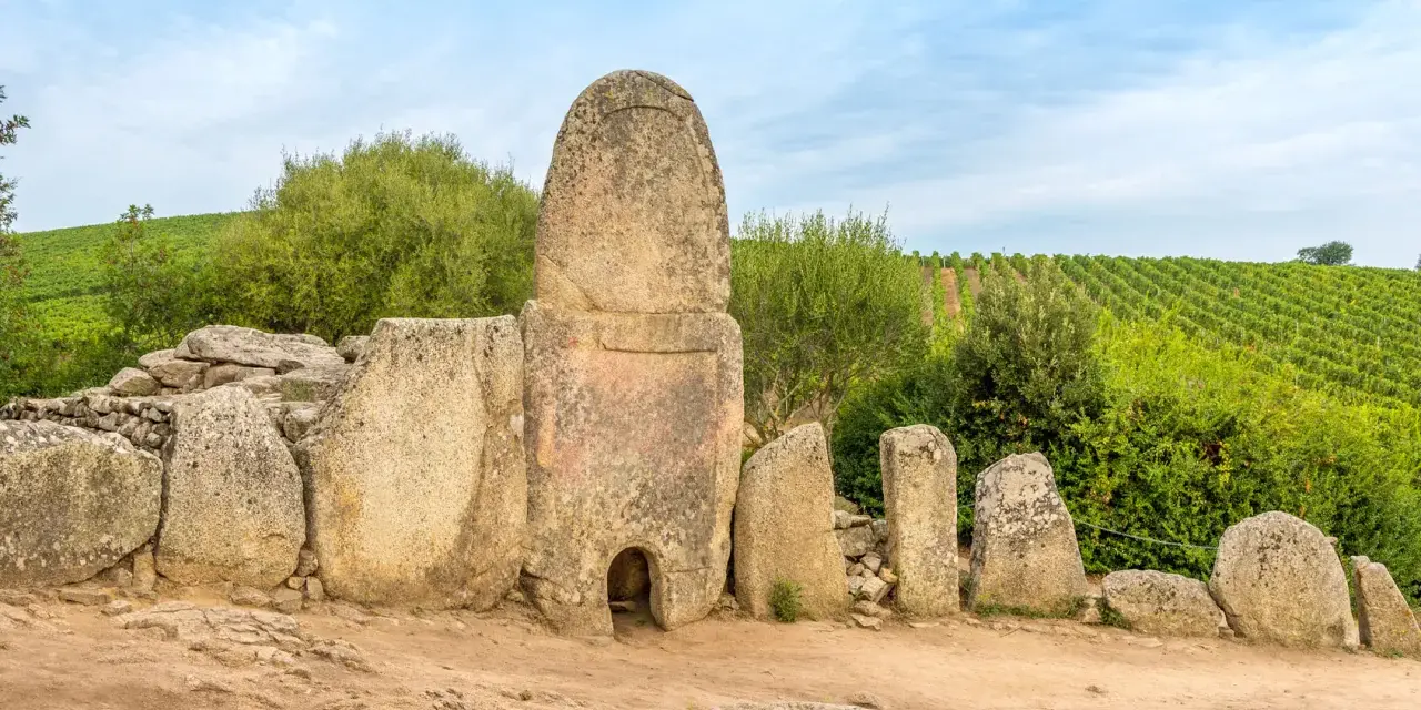 Antiche pietre di un sepolcro a "pozzo" in Sardegna, un vero Stonehenge sardo, circondato da vigneti verdi.