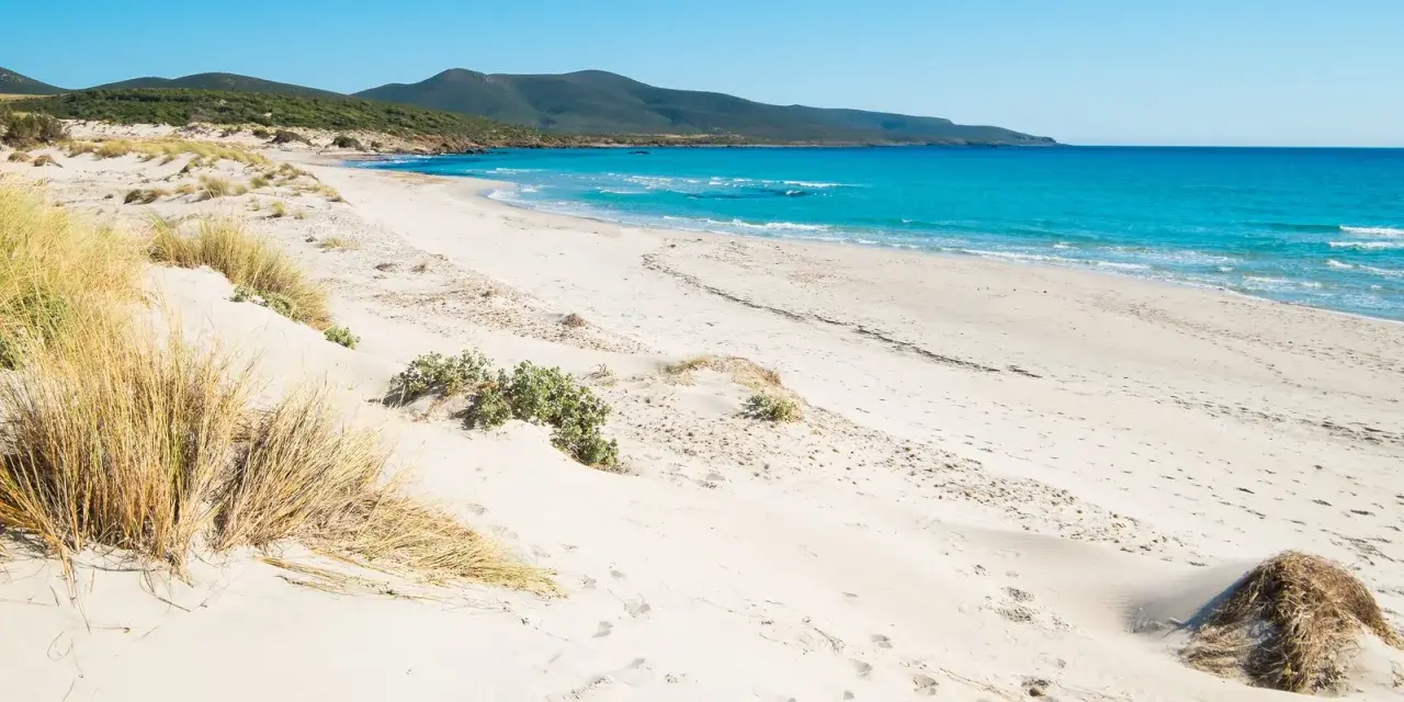 Spiaggia di Porto Pino con dune sabbiose e mare turchese sotto un cielo azzurro.