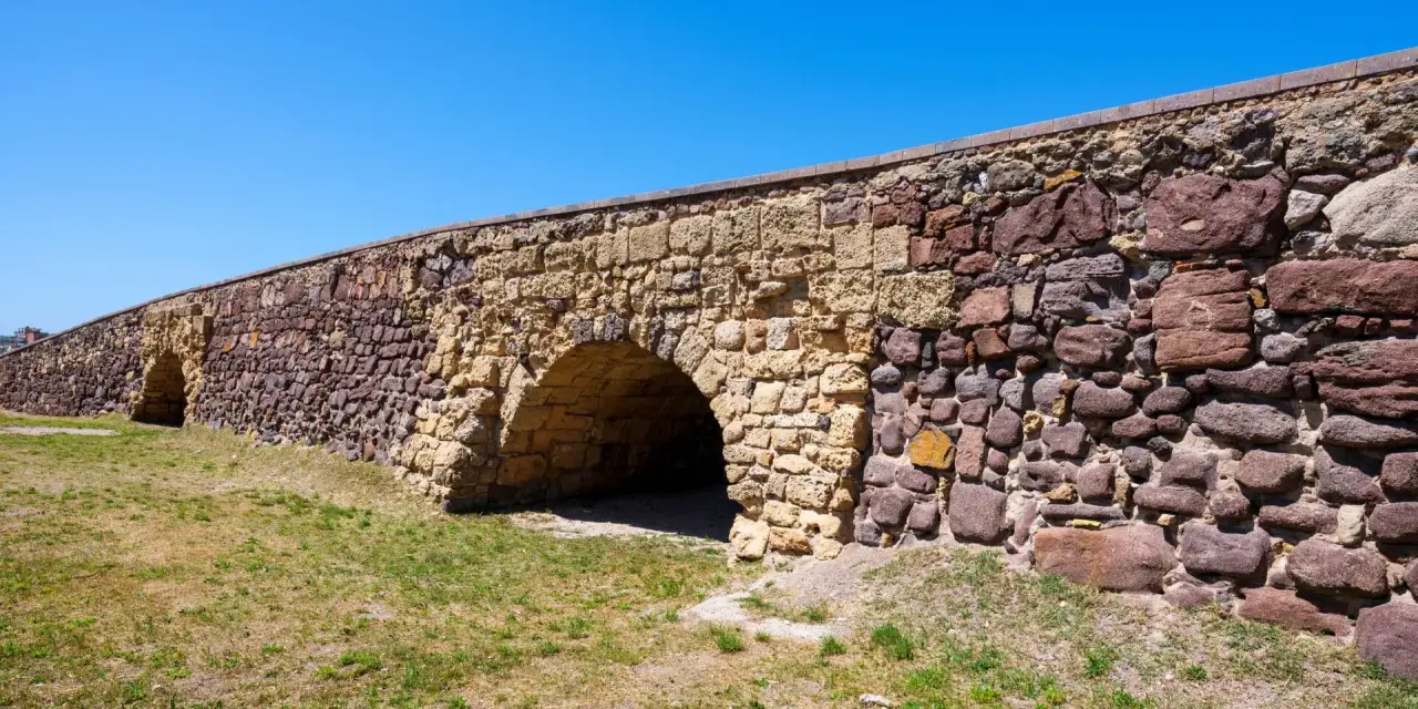 Antico ponte romano a Sant'Antioco, con archi in pietra e un muro imponente sotto un cielo azzurro.